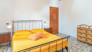 Une chambre à coucher comprenant un lit, une tête de lit en bois, deux tables de chevet, une commode, une armoire en bois et une porte.