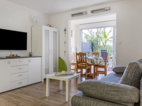 A modern kitchen with white cabinetry, a flat-screen TV, and a dining area with wooden chairs and a table.