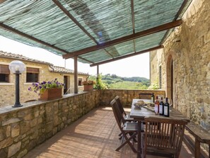 Eine überdachte Terrasse mit Steinmauern, einem Holztisch mit Stühlen und Topfpflanzen.
