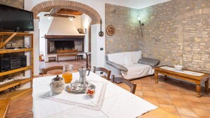 Una sala de estar acogedora con chimenea, paredes de piedra, muebles de madera y un comedor con mesa lista para dos.