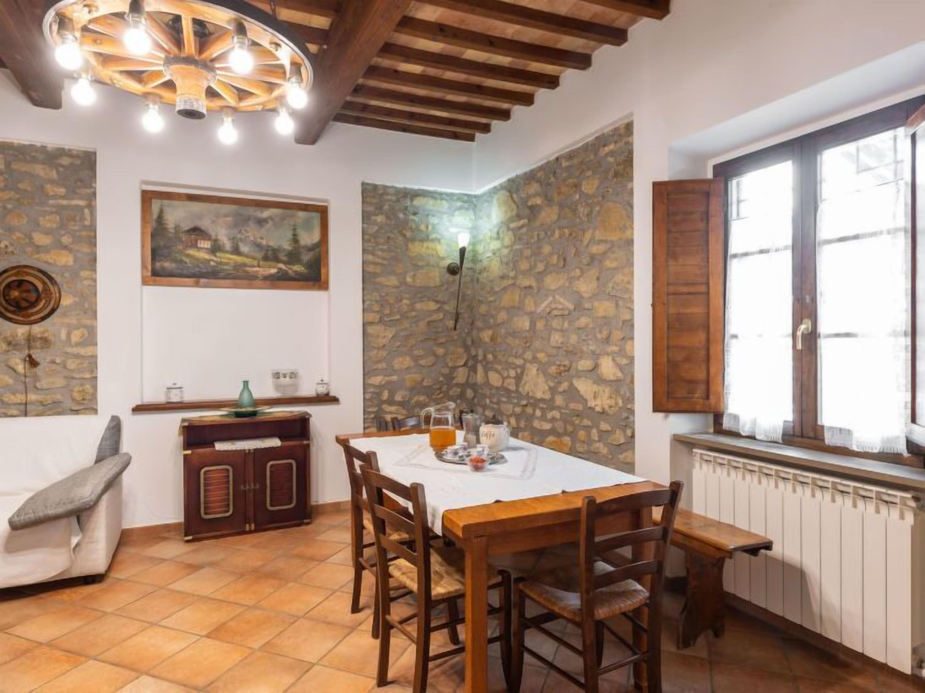 Un coin repas avec une table en bois, des chaises, un tableau et un mur en pierre.