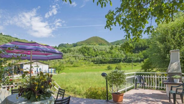 Une terrasse avec une table et des chaises, un parasol violet et une vue sur une vallée verdoyante.