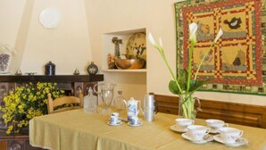 Un coin repas avec une table préparée pour le thé, un vase rempli de fleurs et une courtepointe décorative accrochée au mur.