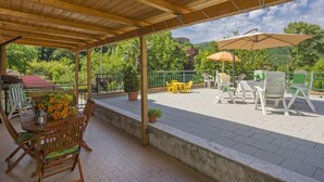 En overdækket terrasse med træbjælker, udendørs møbler og plantekasser.