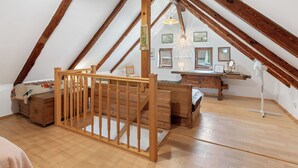 Un dormitorio acogedor en el desván, con vigas de madera, una cuna de madera, un escritorio y un ventanal grande.