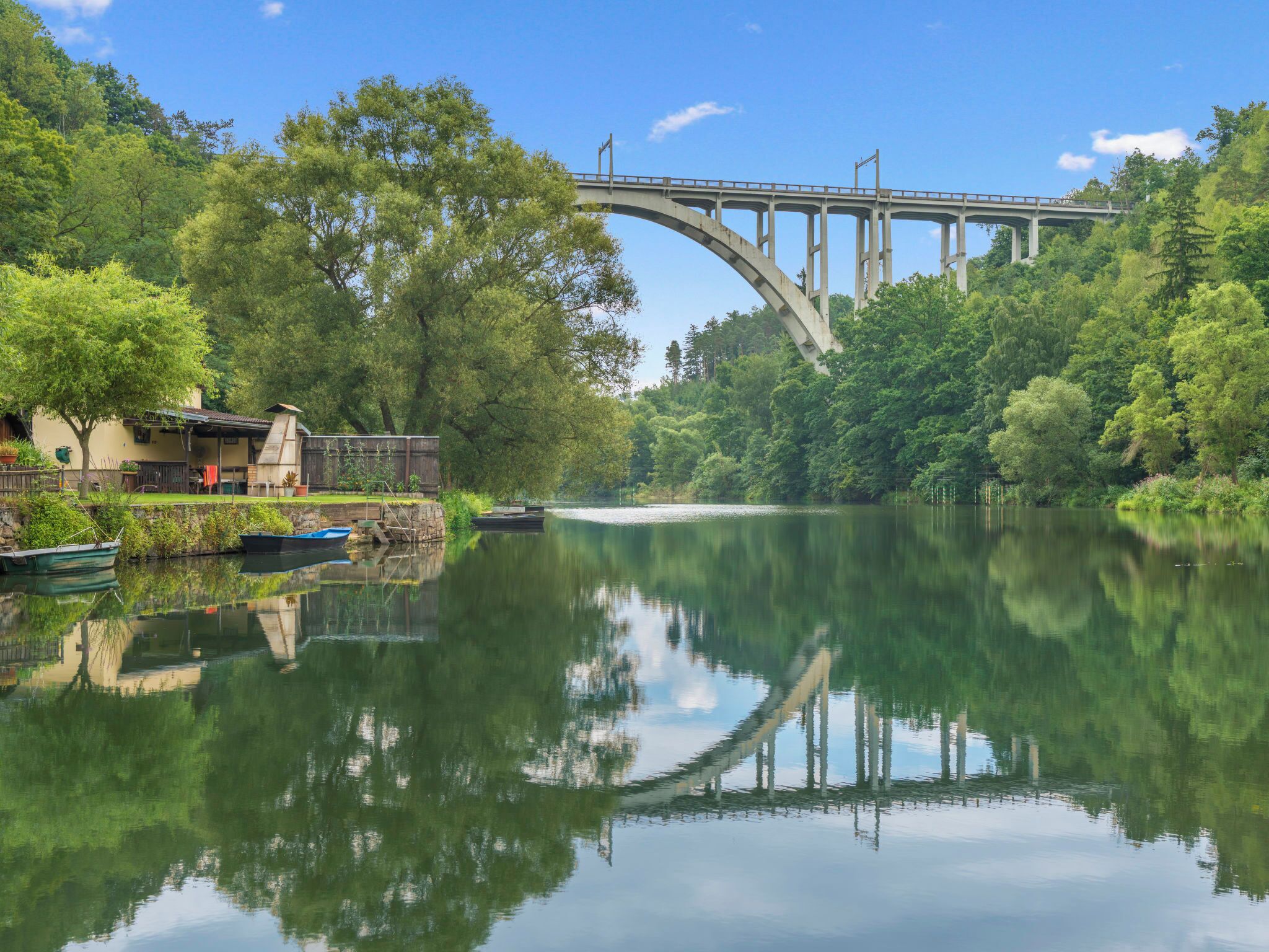 Une rivière avec un pont, des bateaux et une maison dotée d’une terrasse.