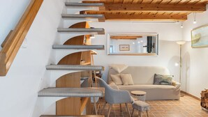 Un interior moderno con una escalera que sube a una zona superior, un conjunto de sofás y una lámpara de pie.