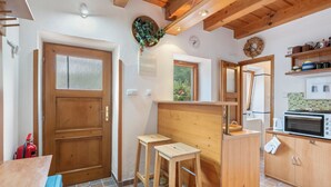 Una cocina compacta con armarios de madera, un microondas y un taburete pequeño.