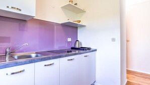 Eine moderne Küche mit weißen Schränken, einer violetten Rückwand und einem Edelstahlspülbecken.