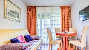 Ein gemütliches Wohnzimmer mit einer Couch, zwei Sesseln, einem kleinen Tisch und einem Fernseher an der Wand.