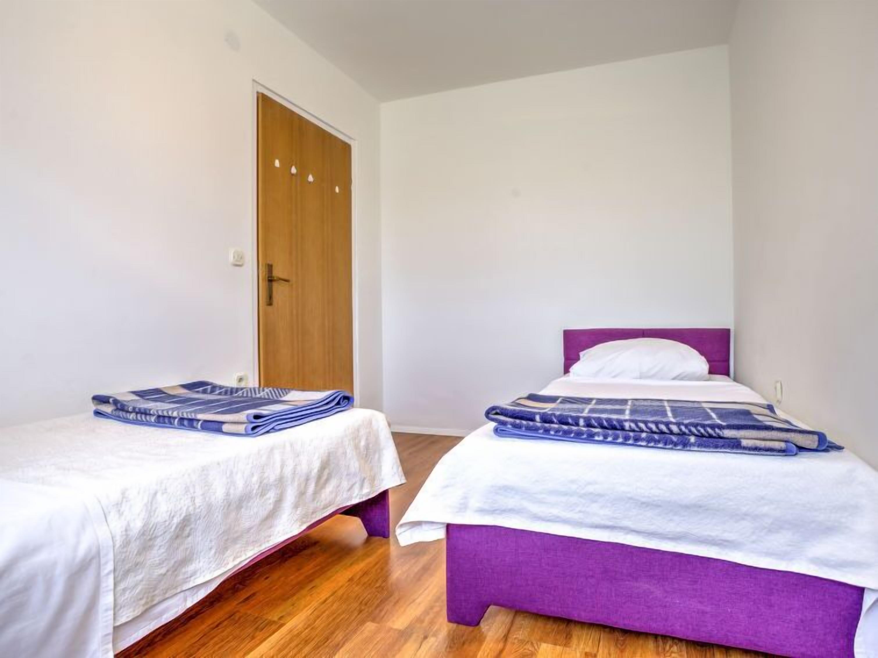 A room with two beds, one with a purple headboard and the other with a white headboard, both with blue blankets.