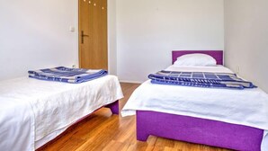 Ein Zimmer mit zwei Betten, eines mit violettem Kopfteil und das andere mit weißem, beide mit blauen Decken.