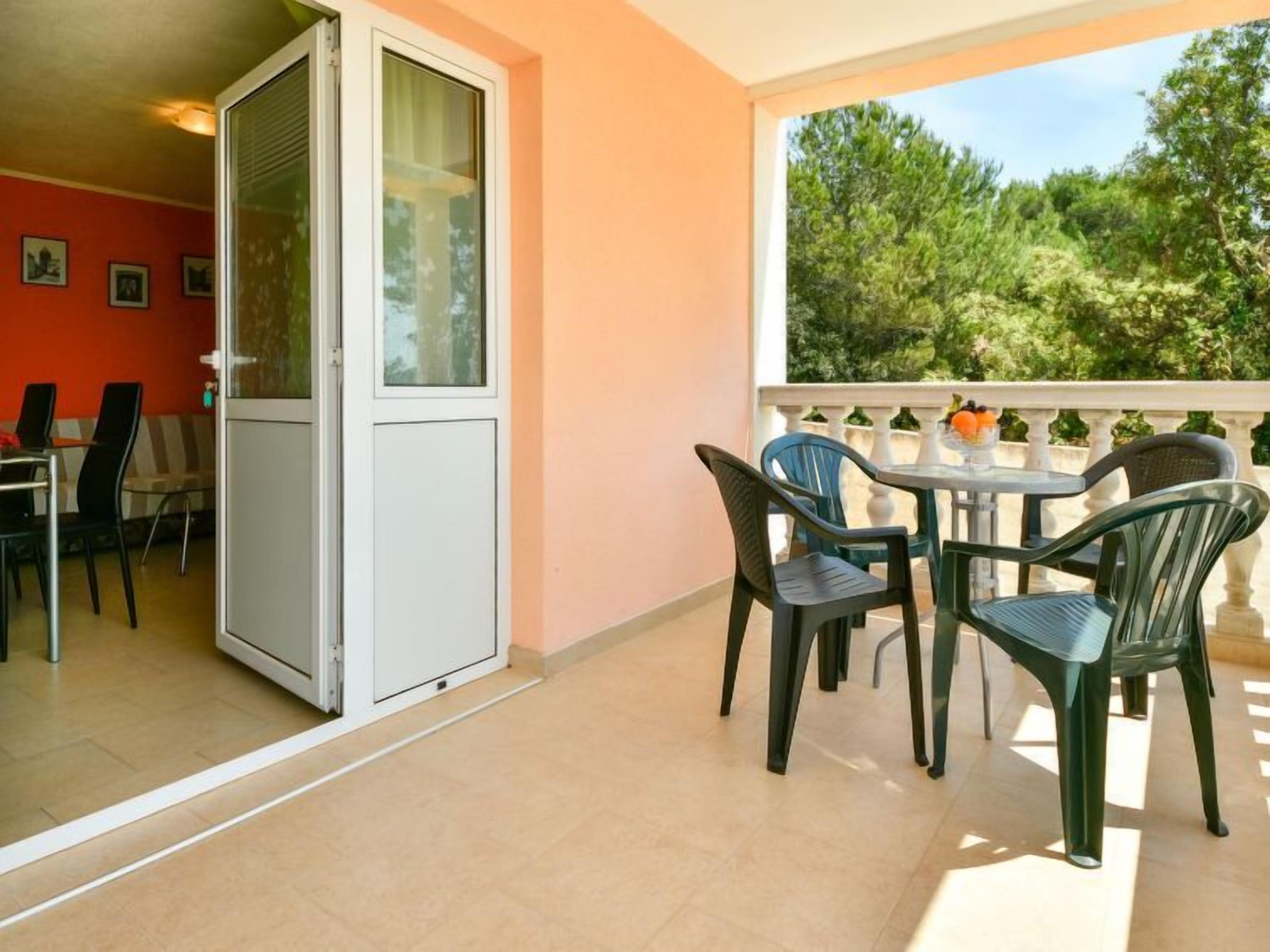 Een balkon met een tafel, stoelen en een glazen schuifdeur, met uitzicht op groen.