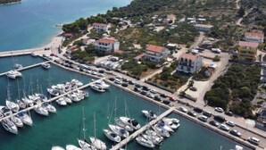 An aerial view of a coastal marina with multiple boats docked, surrounded by residential buildings and a hilly landscape in the background. - Apartment Milin by Interhome (Murter/Jezera)