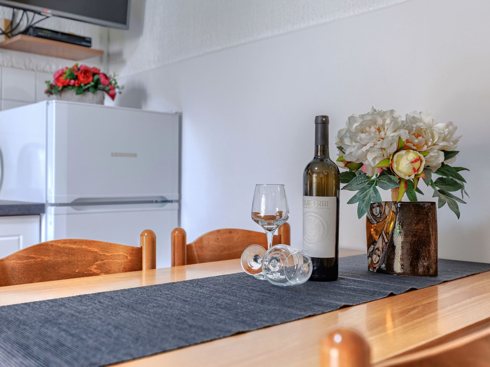 A dining table with a wine bottle, glasses, and a vase of flowers.