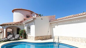 A swimming pool with lounge chairs, a stone wall, and a building with a tiled roof.
