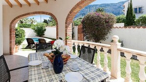 A patio with a table set for dining, surrounded by brick arches and a view of a pool and mountains.