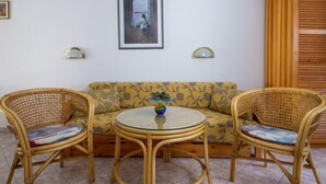 Una habitación con un sofá, dos sillones de mimbre, una mesa de vidrio y dos lámparas de pared.