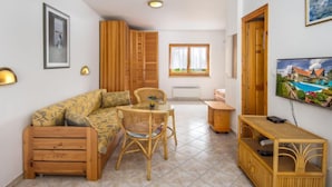 Una sala de estar acogedora con un sofá, una mesa de comedor y un televisor. Se ve una ventana con cortinas y un cuadro en la pared.