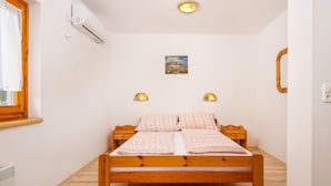 Un dormitorio con una cama de madera, dos lámparas fijadas a la pared, un cuadro pequeño y un ventanal con cortinas.