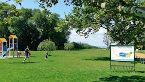 Un parque con un parque infantil, un césped y un cartel.