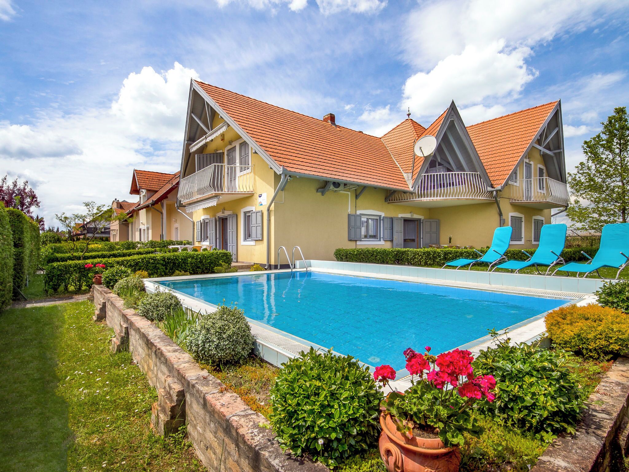 Ein zweistöckiges Gebäude mit Schwimmbad, blauen Liegestühlen und einem gepflegten Garten.