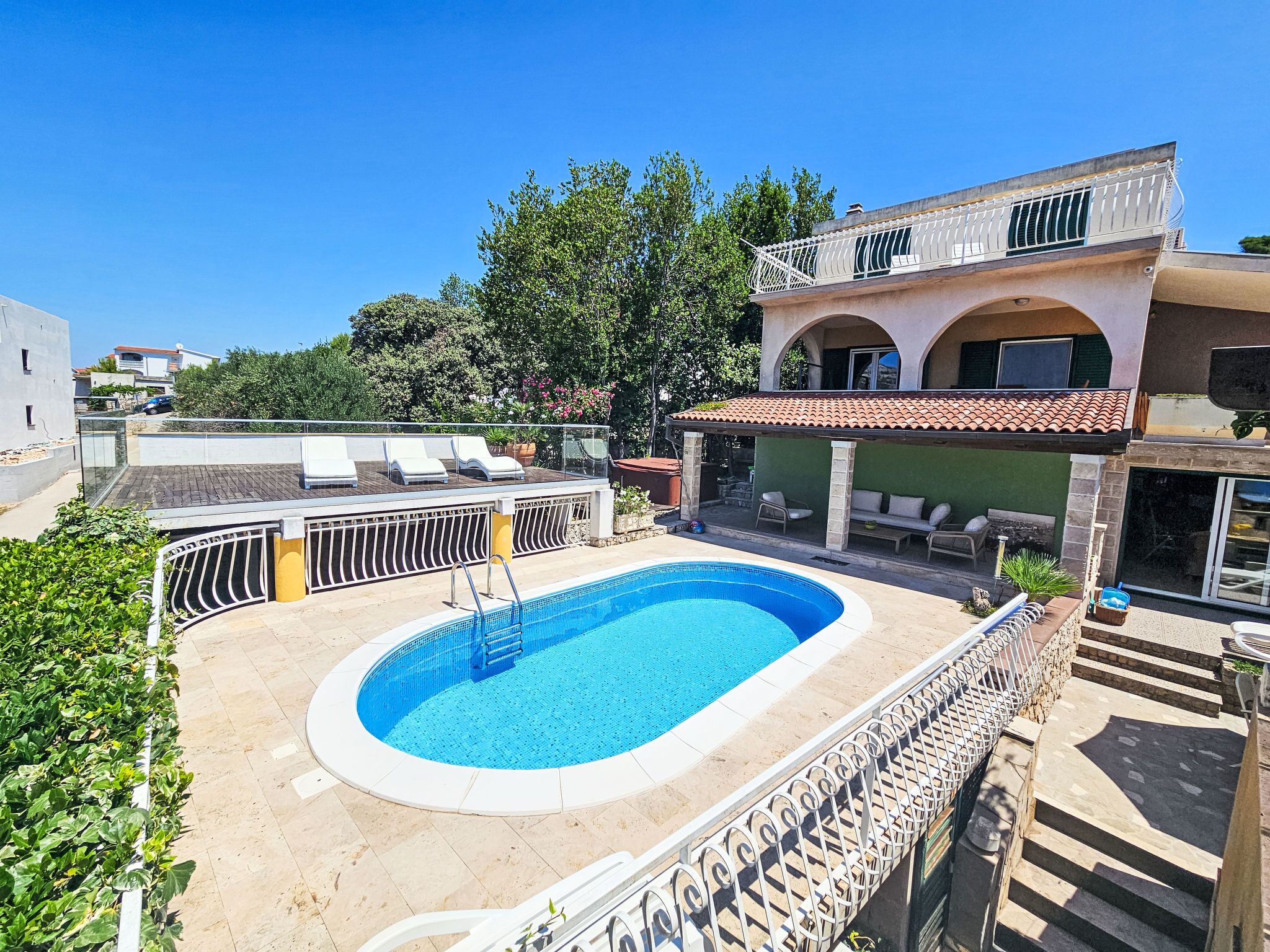 A swimming pool with a sun terrace, lounge chairs, and a covered seating area.