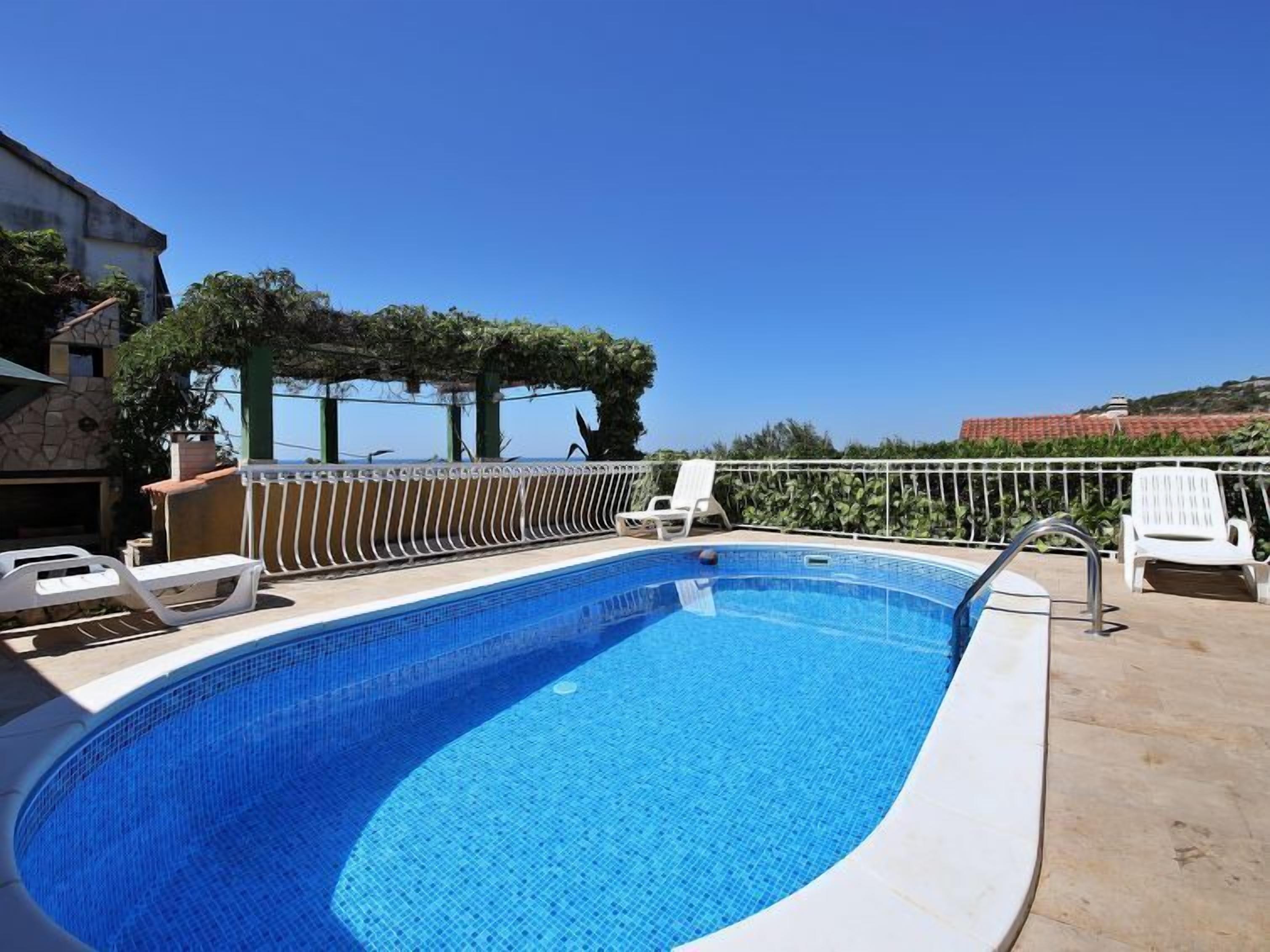 A swimming pool with a clear blue water, surrounded by white lounge chairs and a white fence.