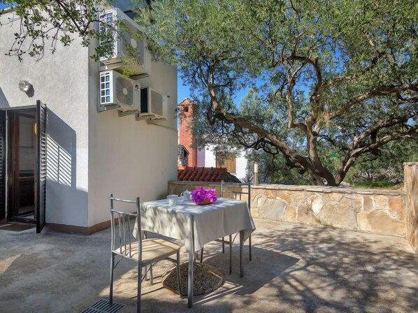 Un espace de restauration en plein air avec une table et des chaises, un mur en pierre et un arbre qui offre de l’ombre.