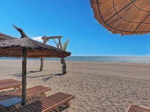 Ein Strand mit Holzliegen und einem Reetdachschirm.