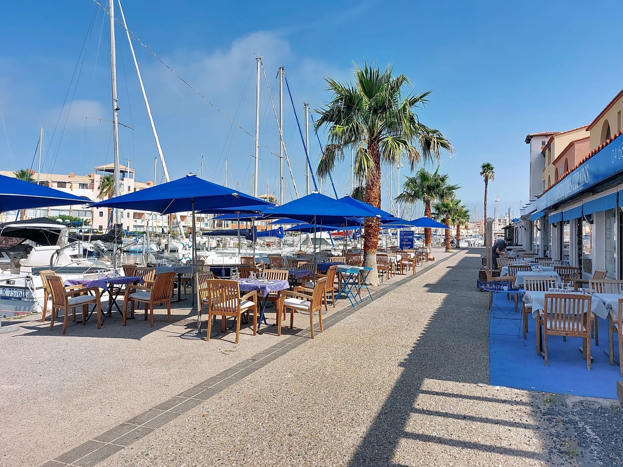 Un port de plaisance avec des bateaux, des parasols bleus et des espaces de détente en plein air.