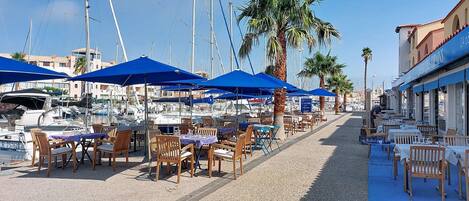 Un port de plaisance avec des bateaux, des parasols bleus et des espaces de détente en plein air.