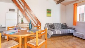 Un salon chaleureux avec une table à manger en bois, des chaises, un canapé et un coin cuisine équipé d’un réfrigérateur.