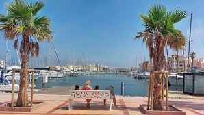Un port de plaisance avec des bateaux, des palmiers et un banc où sont assis des gens.