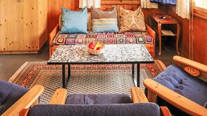A cozy cabin-style room with a wooden interior, a sofa with patterned cushions, a table with a woven placemat, and a television on the wall. - Vacation home Mungg by Interhome (Nendaz)