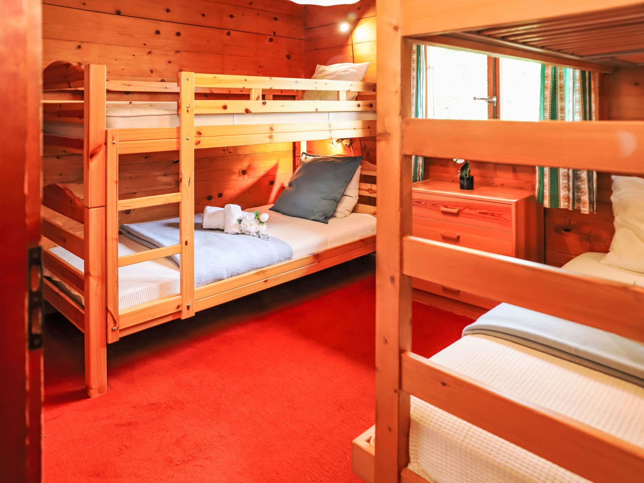 A bunk bed room with a red carpet, wooden walls, and a small bedside table with a bottle.