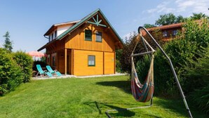 Ein Holzhaus mit geneigtem Dach, einer Hängematte und einem Rasen mit zwei blauen Liegestühlen.