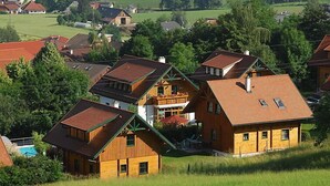 Eine Gruppe Holzhäuser mit geneigten Dächern, umgeben von üppigem Grün und Feldern.