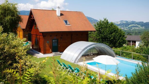 Eine Holzhütte mit rotem Dach, einem Swimmingpool und einem Gewächshaus.