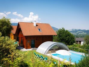 Eine Holzhütte mit rotem Dach, einem Swimmingpool und einem Gewächshaus.