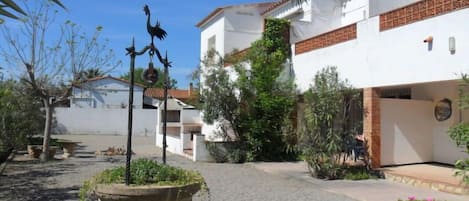 A courtyard with a white building, a stone planter with greenery, and a decorative metal sculpture.