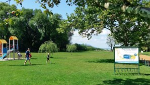 Ein Park mit Spielplatz, einer Rasenfläche und einem Hinweisschild.