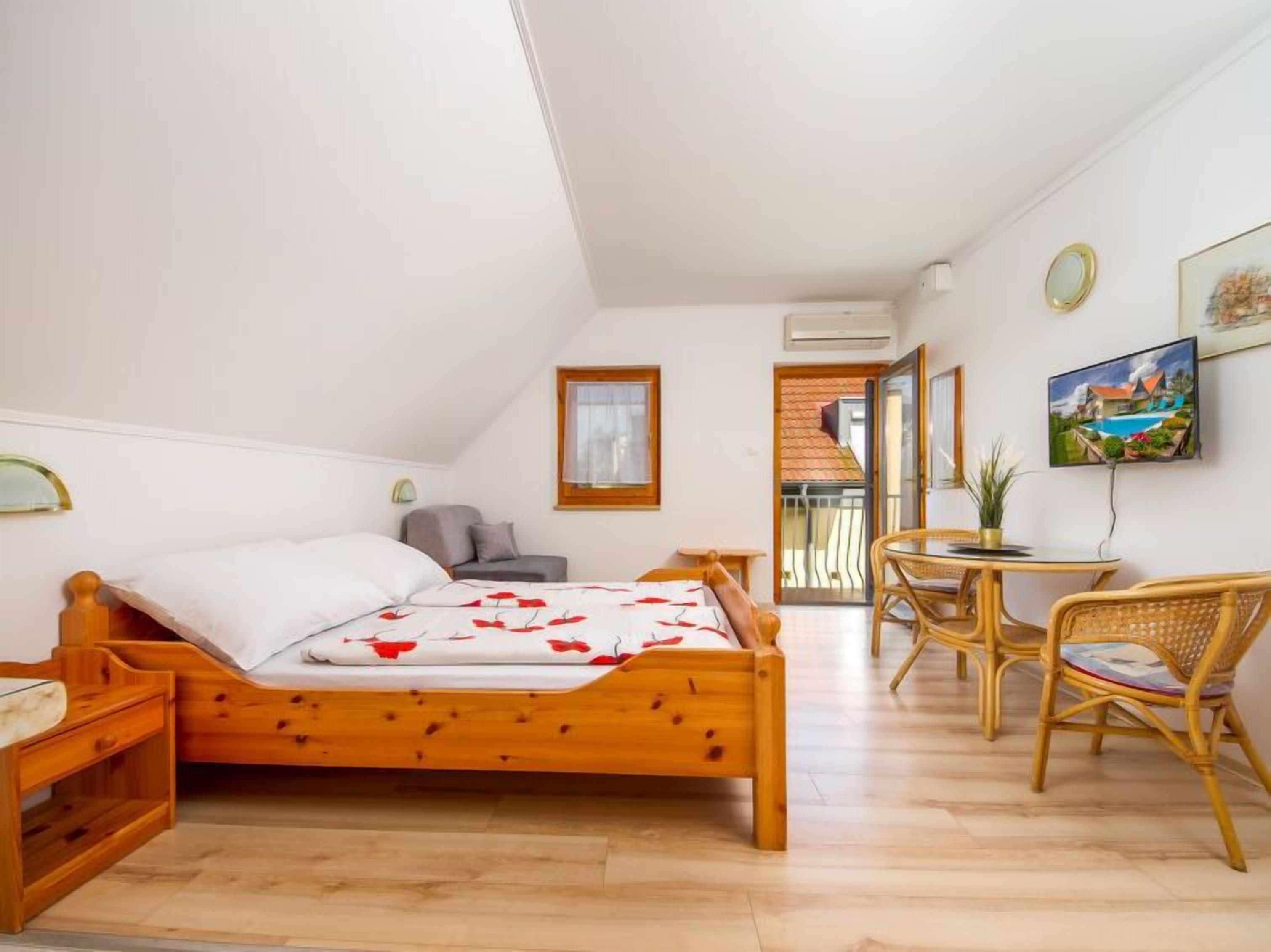 Une chambre avec un lit en bois, une petite table avec des chaises, une télévision et un balcon avec vue.