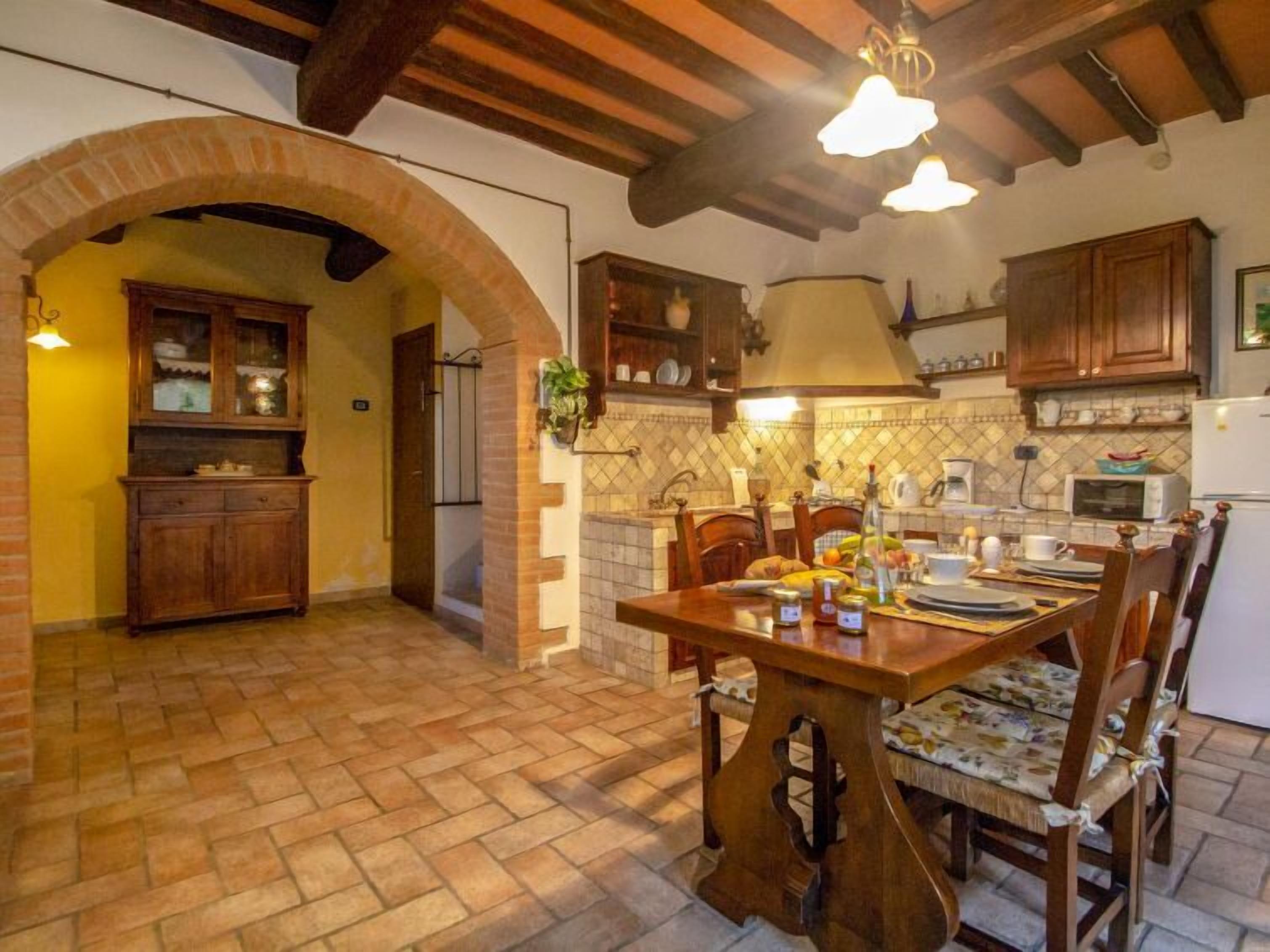 Una cucina rustica con travi a vista, un arco in mattoni, mobili in legno e un'area pranzo con tavolo e sedie.