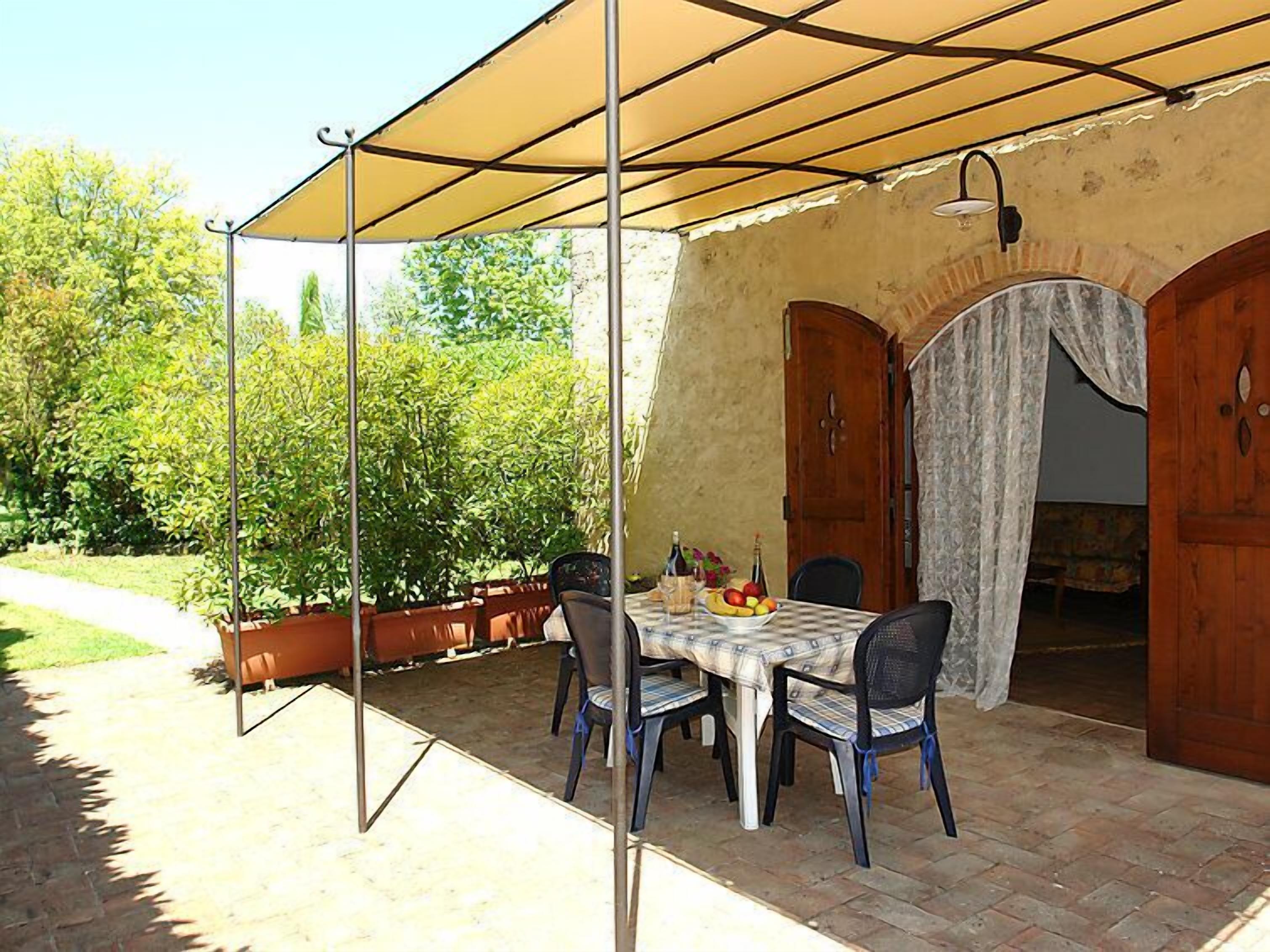 Patio esterno con tavolo apparecchiato per quattro, circondato da sedie, sotto una tettoia.