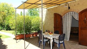 Eine Terrassengruppe im Freien mit einem Tisch für vier Personen, umgeben von Stühlen, unter einem Sonnensegel.