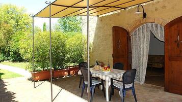 Patio esterno con tavolo apparecchiato per quattro, circondato da sedie, sotto una tettoia.