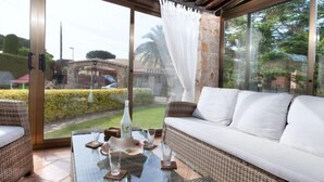 A glass-enclosed patio with a wicker sofa and a glass coffee table. - Origami by Interhome (Calonge)