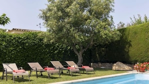 A swimming pool with lounge chairs and a large tree in the background. - Origami by Interhome (Calonge)