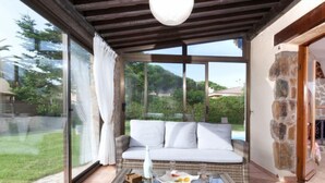A sunlit patio with wicker furniture, a glass table, and a view of a green landscape. - Origami by Interhome (Calonge)